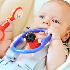 Bambino con sonaglio rosso in mano e gioco blu in bocca, esplora il mondo con i sensi. Ottimo per stimolare neonato ad afferrare oggetti.