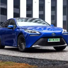 Niebieski samochód na wodór, Toyota Mirai, parkuje przed nowoczesnym budynkiem.