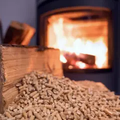 Un poêle à bois Prime Renov crache des flammes chaleureuses. Devant, une bûche et des granulés de bois attendent d'être utilisés.