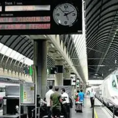 Un tren de alta velocidad espera en la estación. El panel de información muestra un destino a Valencia y Sevilla.