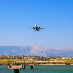 Airplane ascending over a coastal town near the Sicily airport, with mountains in the background.