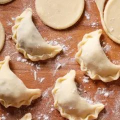 Surowe pierogi z kaszą gryczaną i twarogiem na drewnianej desce, posypane mąką.