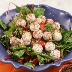 En blå skål med en sallad av gröna blad, körsbärstomater och små, kryddade labneh bollar.