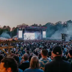 Stor publik vid Rosendal Garden Party. En stor scen med artister och ljusspel, omgiven av träd och tält.