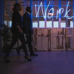 Ludzie idą w stronę neonu "Work", symbolizującego misję i wizję firmy.