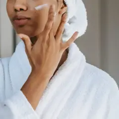 Mujer aplicándose crema en la mejilla, combatiendo los síntomas de la falta de colágeno.
