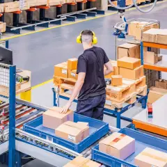 Ein Mitarbeiter mit Kopfhörern sortiert Pakete in einem Lager. Hier wird alles **assemble to order** für den Versand vorbereitet.