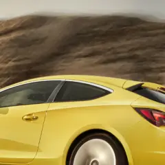 Żółty Opel Astra GTC pędzi przez pustynny krajobraz, zostawiając za sobą smugę kurzu.
