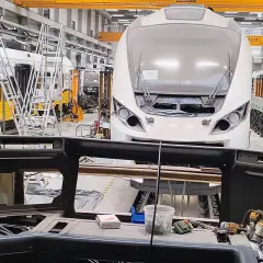 Wykaz pojazdów kolejowych w składzie pociągu w hali produkcyjnej. Widoczne są lokomotywy i wagony w trakcie budowy.