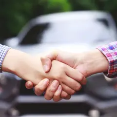 Uścisk dłoni na tle samochodu symbolizuje finalizację umowy, np. cesja leasingu koszty.