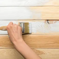 Dłoń maluje białą farbą drewnianą boazerię, odświeżając jej wygląd.