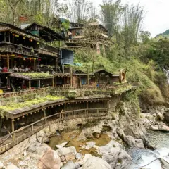 Holzgebäude schmiegen sich an einen Hang in Sapa, Vietnam, mit einem Wasserfall, der daneben herabstürzt.