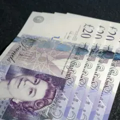 £ co to za waluta? Kilka banknotów po 20 funtów brytyjskich leży na ciemnym tle.