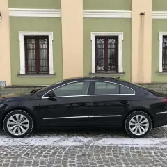 Elegancki, czarny Volkswagen Passat CC na zimowych oponach stoi na ośnieżonej, brukowanej ulicy przed kamienicą z zielonymi oknami.