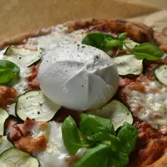 Pyszna pizza z burrata, cukinią i bazylią, posypana świeżo mielonym pieprzem.