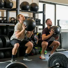 Deux hommes font des squats avec des medecine balls. Un bon sport pour maigrir et se muscler.