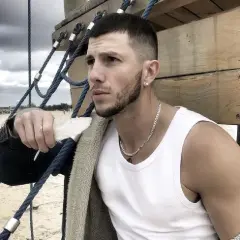 Sasha top model, z piórkiem w dłoni, na tle plaży i chmur.