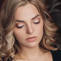 Delikatne, świąteczne makijaże podkreślają urodę blondynki z kręconymi włosami.