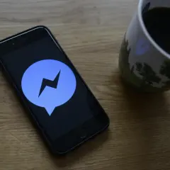 Telefon z ikoną Messengera na ekranie, obok kubek kawy. Dowiedz się, jak ustawić dźwięk powiadomienia Messenger.