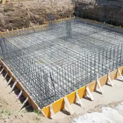 Zbrojenie fundamentów domu w wykopie, otoczone szalunkiem.