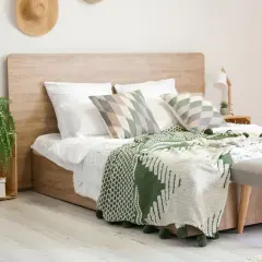 Gemütliches Schlafzimmer mit einem modernen **Aufbau Boxspringbett** in Holzoptik, grünen Decken und Kissen, sowie einer Hängepflanze.