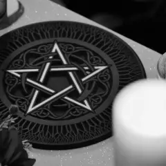 Oto jak wygląda pentagram: pięcioramienna gwiazda wpisana w okrąg, ozdobiona celtyckimi wzorami. Obok świeca w szklanym naczyniu.