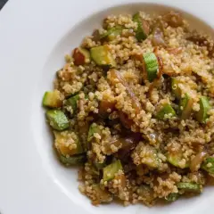 Un piatto di quinoa con verdure, tra cui zucchine a cubetti e cipolle caramellate, servito su un piatto bianco.