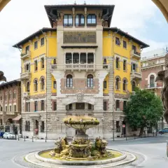 Fontana e palazzo giallo in stile Coppedè, con dettagli scultorei e un'atmosfera d'altri tempi.
