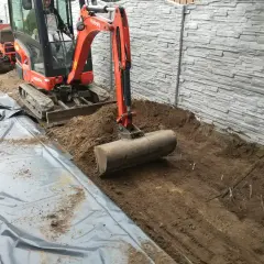 Koparka pracuje nad przygotowaniem terenu pod budowę, usuwając ziemię i przygotowując podłoże.