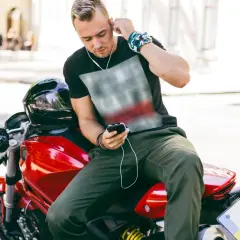 Joven en moto roja ajusta sus auriculares. Disfruta de su música, demostrando que es legal escuchar música en moto.