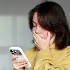 Zaskoczona kobieta zasłania usta dłonią, patrząc na telefon. Czyżby zobaczyła coś niepokojącego, a może to numer 883 co to za numer?