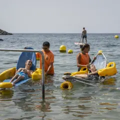 Socorristas ayudan a personas en sillas anfibias en la playa de Aguadulce. Un hombre hace paddle surf al fondo.
