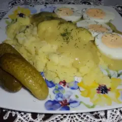 Talerz z ziemniakami puree, jajkami na twardo i ogórkami kiszonymi, polany sosem musztardowym.