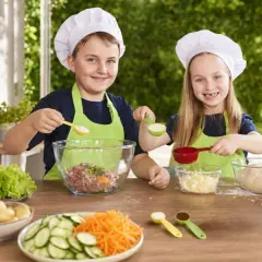 Zwei Kinder mit Kochmützen bereiten sich auf das Grillen vor. Sie mischen Zutaten für Burger und haben Spaß beim gemeinsamen Kochen.
