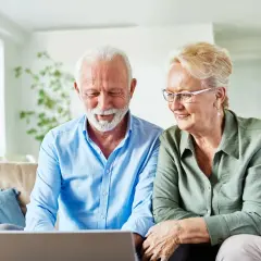 Uśmiechnięta para seniorów sprawdza w internecie, ile wynosi renta inwalidzka w Niemczech.