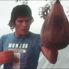 Carlos Monzón, the legendary boxer, trains with a speed bag, his blue shirt bearing his name and the Argentine flag.