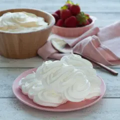 Creme double auf einem rosa Teller, daneben eine Schüssel mit Erdbeeren und ein Holzlöffel.