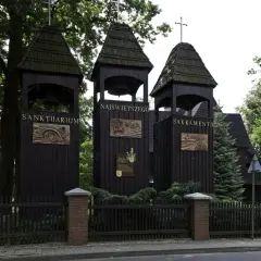 Trzy drewniane dzwonnice przed kościołem w Jankowicach. Na jednej z nich widnieje napis "Sanktuarium Najświętszego Sakramentu".