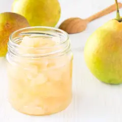 Glas mit Birnenmus, daneben frische Birnen und ein Holzlöffel. Perfekt zum Birnen einkochen.