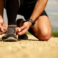 Biegacz na szutrowej drodze zawiązuje buty. Czas na trening, nie ma co czekać, bo "drop co to znaczy" nie ma znaczenia, gdy liczy się ruch.