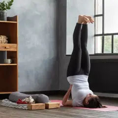 Frau praktiziert Iyengar Yoga in der Umkehrhaltung (Sarvangasana) auf einer rosa Matte, unterstützt von Holzblöcken.