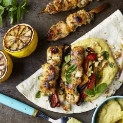 Grillad kyckling kebab med rostade grönsaker och hummus på ett tunnbröd, serverad med grillade citroner och mynta.