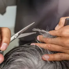 Friseur schneidet kurz grau lila Haare.