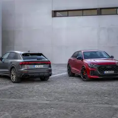 Due Audi RS Q8, una grigia e una rossa, parcheggiate su un selciato di fronte a un edificio moderno.