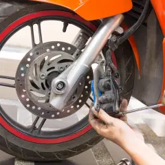 Mecánico ajusta el freno delantero de una moto. Se ve la rueda, disco y pinza de freno.