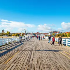 Spacer po drewnianych promenadach nad morzem. Ludzie spacerują, podziwiając widok na plażę i budynki w oddali.