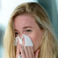 Kobieta z blond włosami używa chusteczki do nosa, aby zatkać nos.