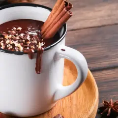 Un déliceux chocolat chaud crémeux, garni de noisettes concassées et de bâtons de cannelle, prêt à réchauffer vos journées.