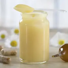 Jalea real para que sirve: frasco con jalea, cápsulas y ampolla, rodeados de flores.