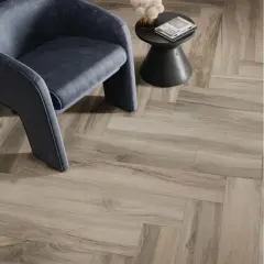 Un fauteuil moderne repose sur un sol en pose carrelage imitation parquet en chevrons, créant une ambiance chaleureuse et élégante.